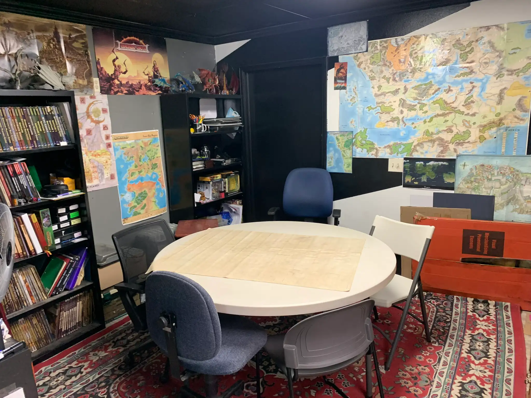A round gaming table beside bookshelves and a big fantasy map